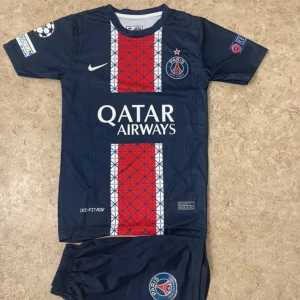 PSG fotbollströja D.Doué #14 Nike - Snygg PSG matchtröja med D.Doué och nummer 14 på ryggen. Tröjan är marinblå med röda och vita detaljer, samt geometriskt mönster framtill. Qatar Airways tryck på bröstet och PSG-logga. Kortärmad och tillverkad i lätt, ventilerande material.