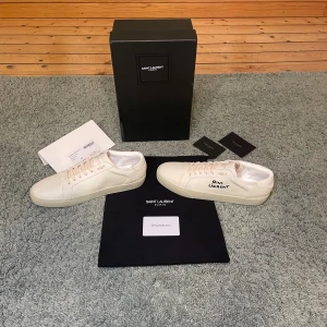 Saint Laurent vita sneakers  - Snygga vita sneakers från Saint Laurent med handskriven logga på sidan. Allt orginal medföljer. Skorna är i storlek 44 och de är helt oanvända.