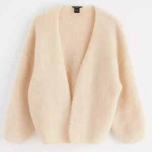 Beige stickad kofta från Lindex - Mysig och fluffig beige stickad kofta från Lindex med avslappnad passform och djup v-ringning. Koftan har långärmade ärmar och är tillverkad i ett mjukt material som känns skönt mot huden. Perfekt att slänga på sig när det är lite kyligt ute. helt slutsåld. storlek M/L sitter oversize.