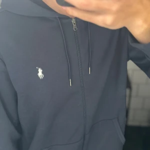 Polo Ralph Lauren zip hoodie - Mörkblå Ralph Lauren zip hoodie i väldigt bra skick, tröjan är snörad i luvan och har en broderad logga på bröstet. Säljer då jag tycker den är för stor. Köpt helt ny från Miinto för runt 1800kr. Priset kan diskuteras o tveka inte på att skriva om ni har några frågor 