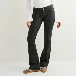 Svarta bootcut byxor med hög midja - Snygga svarta bootcut byxor från Nelly med låg midja och dubbla silverknappar framtill. Byxorna har markerade sömmar längs benen och coola bakfickor med zigzag-detalj. Materialet är stretchigt och ger en smickrande passform. Använd 1 gång