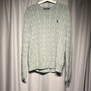 Grå kabelstickad tröja Polo Ralph Lauren - Snygg grå kabelstickad tröja från Polo Ralph Lauren i storlek S. Tröjan har långärmad passform, rund hals och klassisk broderad logga på bröstet. Nypris 2000kr 