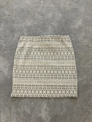 Beige och svart mönstrad kortkjol från Cubus - Snygg kortkjol från Cubus  i beige och svart med ett grafiskt mönster. Kjolen har rak passform och är tillverkad i ett vävt material som känns lite tjockare. Perfekt att matcha med en enkel topp och boots för en cool look.