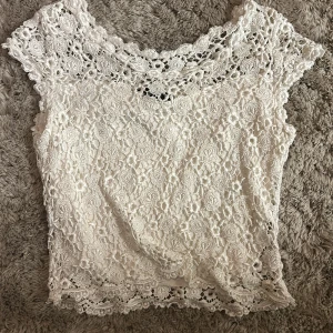 Kort vit spetsblus  - Superfin vit blus i spets med blommigt mönster och korta ärmar. Toppen har en romantisk känsla med detaljerade spetskanter och är perfekt för dig som gillar en söt och feminin look. Står ingen storlek, men skulle gissa på xs 💕