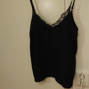 Svart spetslinnetopp från SHEIN - Svart linnetopp från SHEIN i storlek M. Tunt tyg med smala axelband och v-ringning dekorerad med snygg spetskant. Perfekt för lager-på-lager eller att bära som den är. Enkel och stilren design som passar till många outfits.