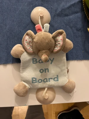Jättefin bilelefant  - Denna produkt är en mjukisdjursskylt med texten 'Baby on Board' och en söt elefantdesign. Perfekt för att fästa i bilen med sugproppar för att visa att du har barn med dig. Produkten ser ut att vara i gott skick utan synligt slitage.