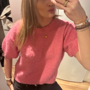 Rosa stickad tröja från Zara - Säljer en superfin rosa stickad tröja från Zara i storlek M. Tröjan har korta ärmar, rund hals och en loose passform som ger en chill vibe. Materialet är mjukt och fluffigt, perfekt för att ge lite färg till din garderob. Passar dig som gillar comfy och trendiga plagg.