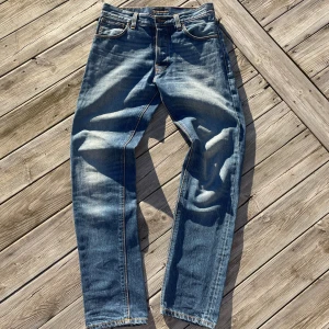 Nudie Jeans Steady Eddie True Classic - Blå jeans från Nudie Jeans, modell Steady Eddie True Classic. Tillverkade i 100% ekologisk bomull med klassisk femficksdesign, orangea sömmar och snyggt slitna detaljer. Rak passform och normal midja, perfekt för en avslappnad stil.