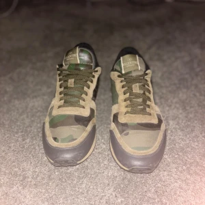 Valentino Rockrunner camo sneakers - Säljer ett par Valentino Rockrunner sneakers med camouflagemönster i grönt, beige och svart. Skorna har detaljer i mocka och skinn, snörning och en cool ljusblå häl. Platt sula och rund tå. Kommer med originalkartong, dustbag och extra skosnören. Små defekter på tån och ena hälen