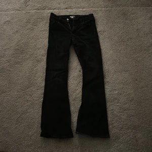 Svarta bootcut jeans  - Säljer ett par svarta jeans från Wrangler med klassisk femficksdesign och bootcut-ben. Jeansen har dragkedja och dubbla knappar i midjan, samt den ikoniska W-sömmen på bakfickan. Materialet är slitstarkt denim och passformen är normal.