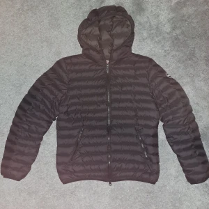 Svart Colmar dunjacka med huva - Svart dunjacka från Colmar med huva och snygga horisontella quiltade sömmar. Jackan har två dragkedjeförsedda fickor fram och en diskret logga på ärmen. Perfekt för kalla dagar och har en modern, sportig look.  Skriv om ni har funderingar eller prisförslag. Storlek 166/ 14 y