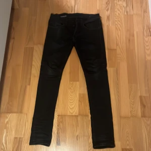 Svarta skinny jeans från Dondup - Svarta jeans från Dondup, modell George Skinny Fit. Snyggt smal passform med klassiska fem fickor och knappgylf. Jeansen har en lätt glansig finish och är tillverkade i stretchigt denim för extra komfort. Perfekt för dig som gillar en modern och stilren look.