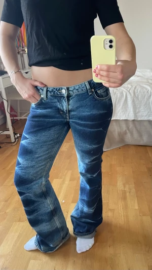 Blå bootcut jeans med låg midja - Säljer ett par blå jeans med coola slitningar och bootcut-ben. De har låg midja och klassisk femficksdesign. De är köpta på weekday. Använd ett fåtal gånger 