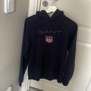 Mörkblå hoodie från GANT med tryck -  mörkblå hoodie från GANT. Andvänd några gånger. Säljer den pågrund av att den är för liten för mig 