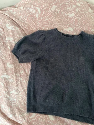 Mörkgrå stickad tröja Vero Moda - Mysig mörkgrå stickad tröja från Vero Moda med kort puffärm och rund hals. Tröjan har ribbade muddar vid nederkant och ärmar, vilket ger en snygg och enkel look. Perfekt för dig som gillar basic med en twist. Den har en liten ljusare fläck som syns på bilderna, har ej försökt få bort fläcken, men därav det låga priset! Använd ett fåtal gånger! 