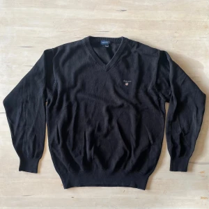 Svart stickad v-ringad tröja GANT - Svart stickad tröja från GANT i storlek S med v-ringad hals och diskret broderad logga på bröstet. Tröjan har långa ärmar och ribbade muddar vid ärmslut och nederkant. Perfekt för dig som gillar klassisk och stilren look.