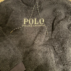 Mörkgrå fleece hoodie Polo Ralph Lauren - Säljer en mörkblå hoodie från Polo Ralph Lauren i supermjuk fleece. Tröjan har huva med snörning och stor logga framtill. Perfekt för dig som gillar chill och streetwear-vibe. Passar dig som vill ha en oversized look och gillar fluffigt material. Och även extrem skön till vintern