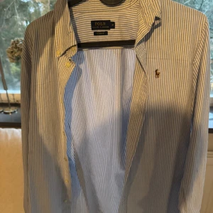 Blårandig skjorta från Polo Ralph Lauren - säljer detta föe att min små storlek till min killw! Snygg blårandig skjorta från Polo Ralph Lauren med klassisk krage och knappar framtill. Skjortan har lång ärm och det ikoniska broderade logot på bröstet. Tillverkad i mjuk bomull som känns skön mot huden. Perfekt för dig som gillar stilrena och tidlösa plagg.