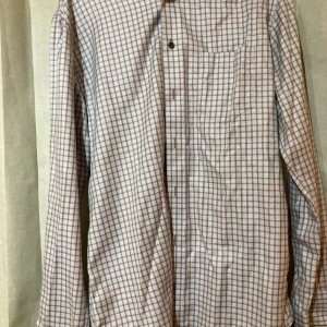 Rutig skjorta från Oscar of Sweden- NY - Klassisk rutig skjorta från Oscar of Sweden i beige och vitt. Skjortan har lång ärm, bröstficka och knappar framtill. Regular fit och mjukt bomullstyg gör den både snygg och bekväm. Perfekt för dig som gillar stilren och tidlös design.