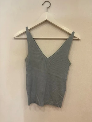 Blå ribbad linnetopp med v-ringning - Snygg blå linnetopp med breda axelband och djup v-ringning. Toppen är ribbad och har en croppad passform som ger en modern vibe. Perfekt att styla med jeans eller kjol för en chill look. Materialet känns mjukt och stretchigt.