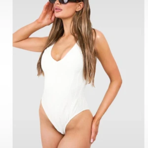 Vit baddräkt från Boohoo - Supersnygg vit baddräkt från Boohoo med rynkad struktur och djup v-ringning både fram och bak. Hög skärning vid benen ger en trendig look. Perfekt för stranden eller poolen, enkel att matcha med en sarong eller shorts. Har tvättat den därav är plomberingen borta men den var alldeles för liten på mig så väljer att sälja den. Helt oanvänd! Lånade bilder