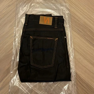Helt nya Nudie jeans co - grim Tim - W30 L32 - Helt nya och oanvända Nudie Jeans Co Grim Tim i den exklusiva färgen Dry Black Coated – fortfarande i originalförpackning (se bilder).  Detta är en av Nudies mest populära modeller, med en tidlös passform och den välkända premiumkvaliteten som gör Nudie till ett av Sveriges mest uppskattade jeansmärken.  Nypris: 1600  Detaljer: • Modell: Grim Tim • Storlek: W30 / L32 • Färg: Dry Black Coated (svart med lätt glans och vaxad look) • Passform: Regular slim fit – normal midja, rakare ben