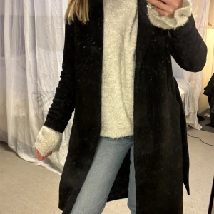 Svart kappa med bälte från Vero Moda - Svart lång kappa från Vero Moda i storlek XS. Lite nopprig, men går att få bort med rakhyvel 🤗