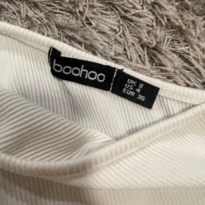Vit oneshoulder croppad topp Boohoo - Säljer en vit ribbad oneshoulder topp från Boohoo i croppad modell. Toppen har en lång ärm på ena sidan och är axelbandslös på andra, vilket ger en cool asymmetrisk look. Perfekt för dig som gillar trendiga och stilrena plagg.  Storlek 36