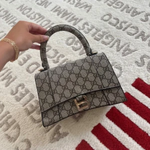 Gucci handväska med monogrammönster - Snygg handväska från Gucci i klassiskt monogrammönster. Väskan är beige och brun med GG-logga över hela ytan, har ett stadigt handtag och medföljande axelrem. Stängs med ett guldfärgat spänne framtill. Perfekt för dig som vill ha en ikonisk och trendig accessoar.