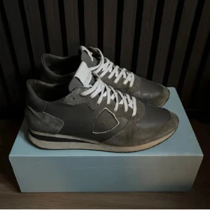 Grå Philippe Model sneakers i mocka och skinn - Snygga sneakers från Philippe Model i grått med vita snören. Skorna har en mix av mocka och skinn, klassisk låg profil och rund tå. Sulan är vit med svart rand och de har märkets logga på sidan. Perfekta för dig som gillar stilrena och exklusiva sneakers.