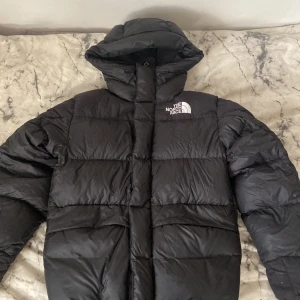 Svart pufferjacka från The North Face XS - Svart pufferjacka från The North Face i storlek XS. Jackan har en stor huva, broderad logga på bröstet och ryggen, samt breda quiltade sektioner. Perfekt för kalla dagar och har en riktigt schysst streetstil. Passar även S. Katthår kan förekomma.