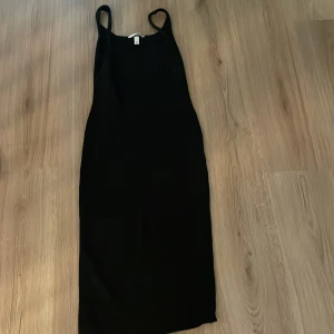 Svart långklänning från H&M XS - Svart långklänning från H&M i storlek XS. Klänningen har smala axelband och en rak, figurnära siluett som ger en stilren look. Knappt använd och hör av er om ni har några frågor💕
