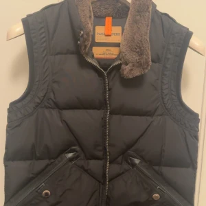 Svart dunväst från Parajumpers - Svart dunväst från Parajumpers med slim fit och fluffig krage i brunt. Västen har två snedställda fickor med dragkedja och detaljer i svart skinn. Perfekt för kalla dagar. Nypris: 4000kr+