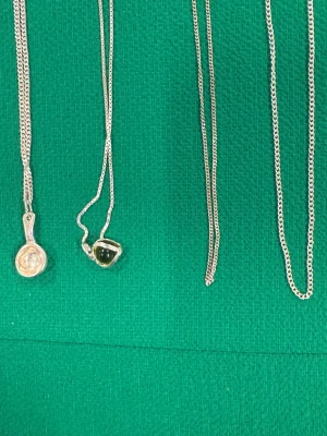 Fyra silverhalsband med hängen - Säljer fyra stilrena silverhalsband. Två av kedjorna har unika hängen: ett med rund, guldtonad detalj och ett med mörkgrön sten infattad i silver. De andra två är enkla kedjor utan hänge. Perfekt för dig som gillar minimalistisk och cool stil.