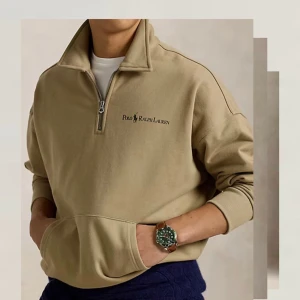 Beige half zip sweatshirt Polo Ralph Lauren - Snygg beige sweatshirt från Polo Ralph Lauren med half zip med krage. Tröjan har svart logotyp på bröstet, känguruficka och ribbade muddar.  Tillverkad i mjuk bomullsmix, perfekt för chill dagar. Passformen är relaxed och ärmarna är långa.           Nypris 1600kr