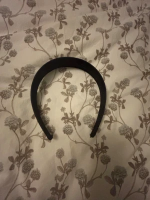 Svart diadem i enkel design - Snyggt svart diadem med klassisk och stilren form. Perfekt för att hålla håret på plats och ge en clean look. Diademet är brett och har en matt finish, vilket gör det lätt att matcha med olika outfits. Materialet känns mjukt och bekvämt mot huvudet.