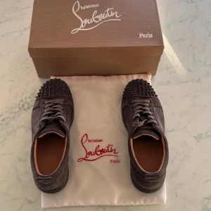 Christian Louboutin grå mocka sneakers - Snygga grå sneakers från Christian Louboutin i mocka med rund tå och platt sula. Skorna har snörning och coola svarta nitar på tån för en edgy vibe. Insidan är i beige skinn och yttersulan är svart. Perfekta för dig som vill sticka ut med lyxig streetstyle. Pris kan diskuteras av snabb affär👍
