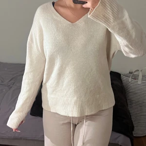 Beige stickad v-ringad tröja - Mysig beige stickad tröja med v-ringning och långa ärmar. Tröjan har breda ribbade muddar vid ärmslut och nederkant, vilket ger en chill och avslappnad vibe. Perfekt för att hålla sig varm under kyliga dagar.
