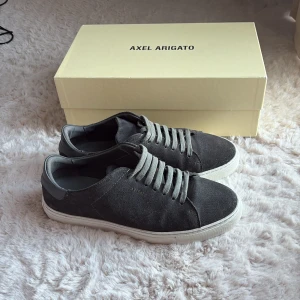 Grå mocka sneakers Axel Arigato - Snygga grå sneakers från Axel Arigato med ovandel i mocka och vita platta gummisulor. Skorna har rund tå, grå snörning och diskret logga på sidan. Perfekt för dig som gillar stilrena och minimalistiska sneakers med premiumkänsla. Ny pris 2600kr. Bara höra av sig vid fundering 🙂