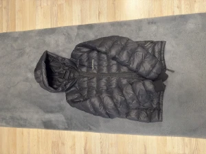 Svart dunjacka från Peak Performance - Jättebra skick! Knappt använd. Säljer en svart/ mörkblå dunjacka från Peak Performance med huva och dragkedja framtill. Jackan har puffad design, ribbade muddar och diskret logga på bröstet. Perfekt för kalla dagar och har en clean, sportig look som funkar till allt. Köpt för 3199 förra året. Kan diskutera om priset