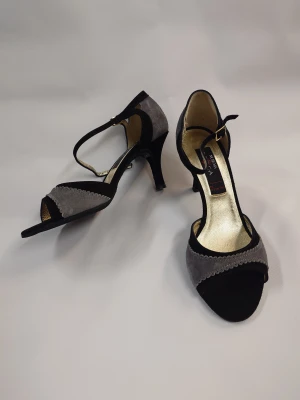 Grå och svarta Danskor med klack - Snygga Dansskor från Nueva Epoca i grått och svart med öppen tå och elegant klack. Skorna har en smal rem med spänne över foten och dekorativ kantdetalj framtill. Insidan är guldfärgad för extra lyxig känsla. Nypris 1500-1800kr