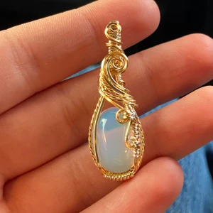 Guldtrådsinlindat berlock med opalit - Unikt halsband med en droppformad opalitsten inlindad i snirklig guldtråd. Stenen skimrar i vitt och blått och ger ett magiskt intryck. Perfekt för dig som gillar boho eller vill ha något som verkligen sticker ut.