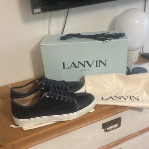 Lavin cap toe - Snygga svarta sneakers från Lanvin med vit platt sula och rund tå. Skorna har snörning och är tillverkade i blankt skinn med en stilren design. Kommer med originalkartong och dustbag. Perfekta för dig som gillar exklusiva och minimalistiska sneakers. Priset går såklart att diskutera om”