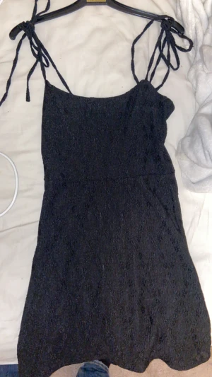 Svart kort klänning med knytband - Supersöt svart kort klänning från H&M med tunna axelband som knyts och så fina mönster i tyget på klänningen. 