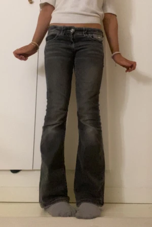 Grå bootcut jeans från Gina Tricot - Snygga grå jeans från Gina Tricot i storlek 146. Modellen har bootcut-ben, låg midja och coola fickdetaljer med knappar bak. Jeansen har klassisk femficksdesign och är tillverkade i mjukt denimtyg med slitningar för en trendig look.