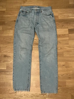 Ljusblå jeans från Lager 157, storlek 28/32 - Säljer ett par ljusblå jeans från Lager 157 med klassisk femficksdesign och raka ben. Jeansen har råa, fransiga benslut och bronsfärgade nitar. Passar dig som gillar en avslappnad och enkel stil. Materialet är slitstarkt denim i bomull.