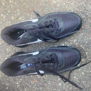 Svarta Nike Air Max sneakers - Nike Air Max sneakers i svart med silvriga detaljer och synlig Air Max-bubbelsula. Ovandelen är i mesh och syntet, med snörning och rund tå. Snygg, sportig look och riktigt skön dämpning i sulan. Perfekt för dig som gillar streetstyle och vill ha något som sticker ut.