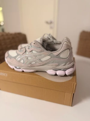 Asics GEL-NYC sneakers i ljusgrått - Säljer ett par Asics GEL-NYC sneakers i en clean ljusgrå och vit färgskala. Skorna har meshpaneler och detaljer i mocka och syntet, samt en chunky sula med dämpning. Perfekta för dig som gillar sportig och trendig stil. Levereras med originalkartong.