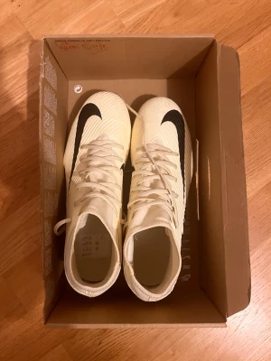 Nike Superfly 9 Club FG/MG fotbollsskor - Säljer ett par Nike Superfly 9 Club FG/MG fotbollsskor i storlek 43. Skorna är ljusgula med svarta detaljer och stora Nike-loggor på sidorna. De har snörning, platt sula med fasta dobbar och är tillverkade i syntetmaterial för bra grepp på planen. Jag har använt de bara 2 gånger och för bara 100kr du kan få benskyddet från Puma. Priset kan diskuteras.