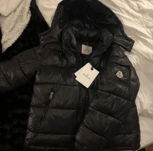 Moncler Maya - Säljer min äkta Moncler-dunjacka i svart. Jackan är varm, lätt och superbekväm – perfekt för höst och vinter. Klassisk Moncler-design med logga på ärmen, huva och två praktiska fickor med dragkedja. Priset går att diskutera!    jackan är i storlek 1 som motsvarar S i ” vanlig” storlek.